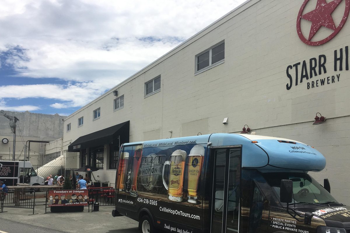 A wrapped Hop On shuttle parked below the Starr Hill Brewery sign, the patio and its guests at left